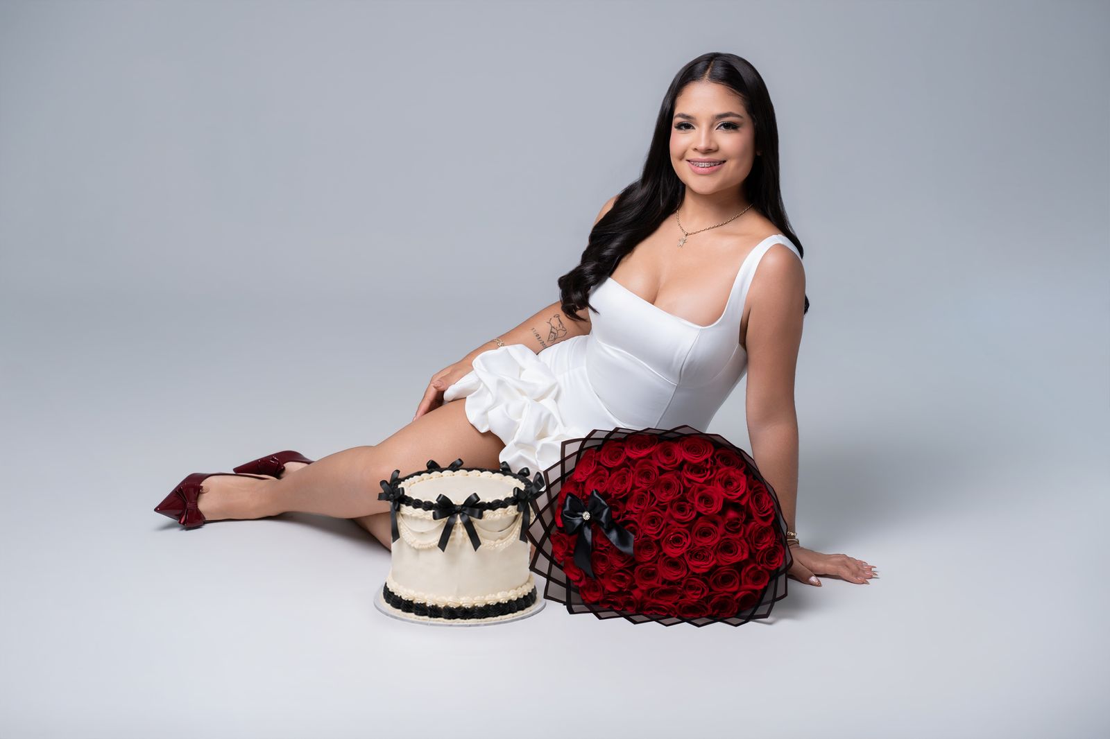 Studio birthday portrait with white cake and a bouquet of red roses