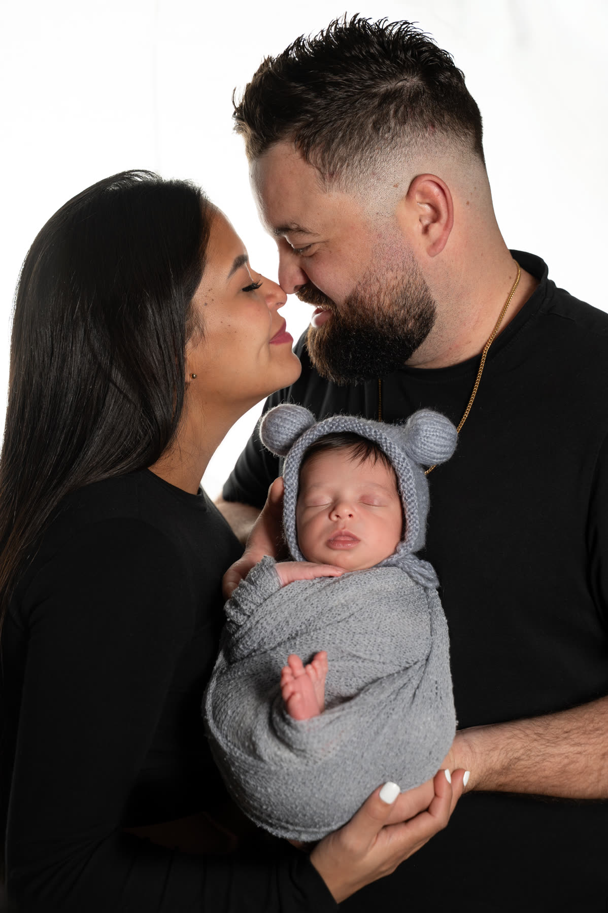 Parents sharing a kiss above their newborn in a bear bonnet
