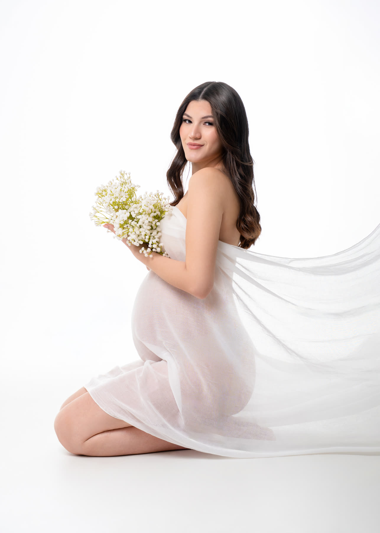Kneeling maternity portrait in white chiffon holding white flowers