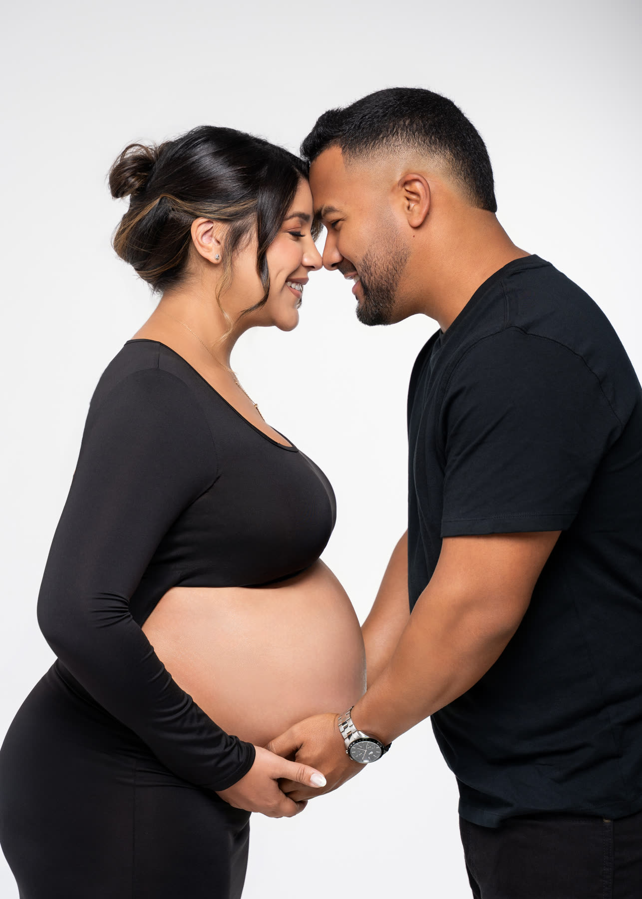Expecting couple forehead to forehead, hands on the belly