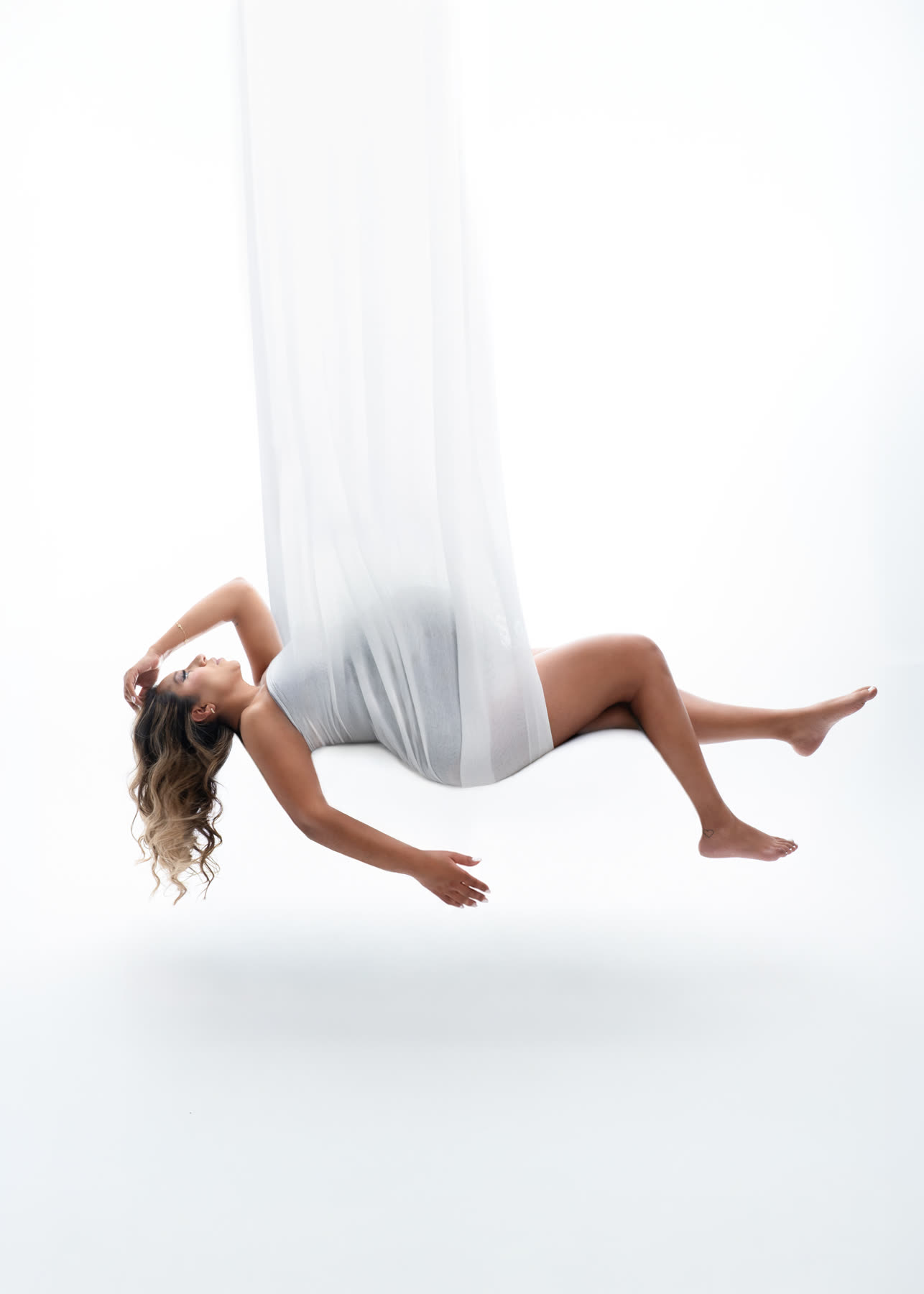 Expectant mother floating in a white silk hammock above the studio floor