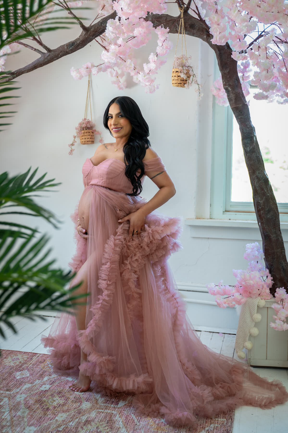 Expectant mother in a pink tulle gown under blossom branches