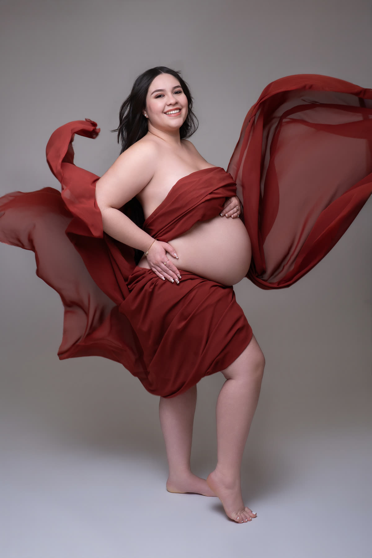 Joyful maternity portrait with red silk in motion