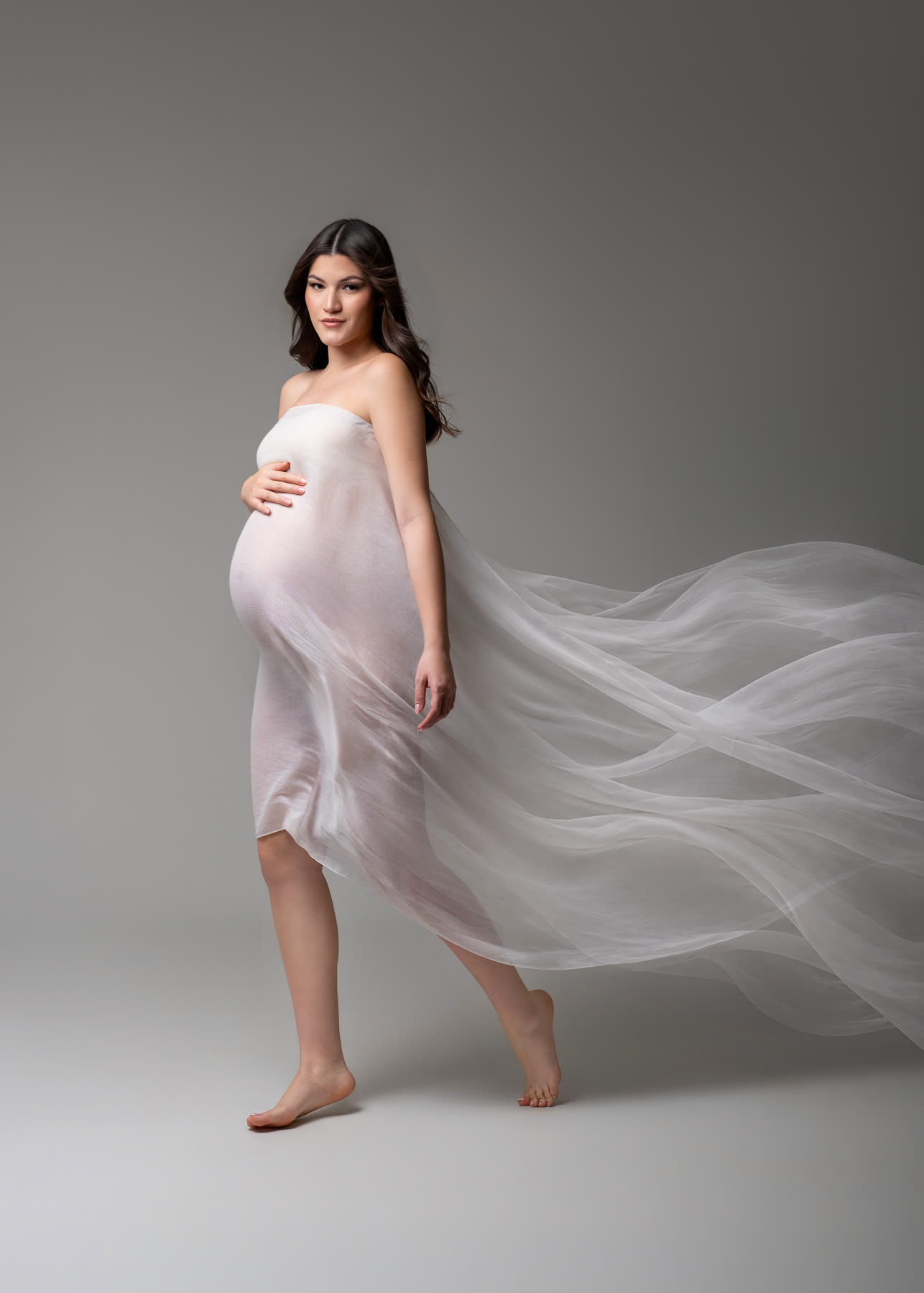 Expectant mother walking with white silk trailing behind her