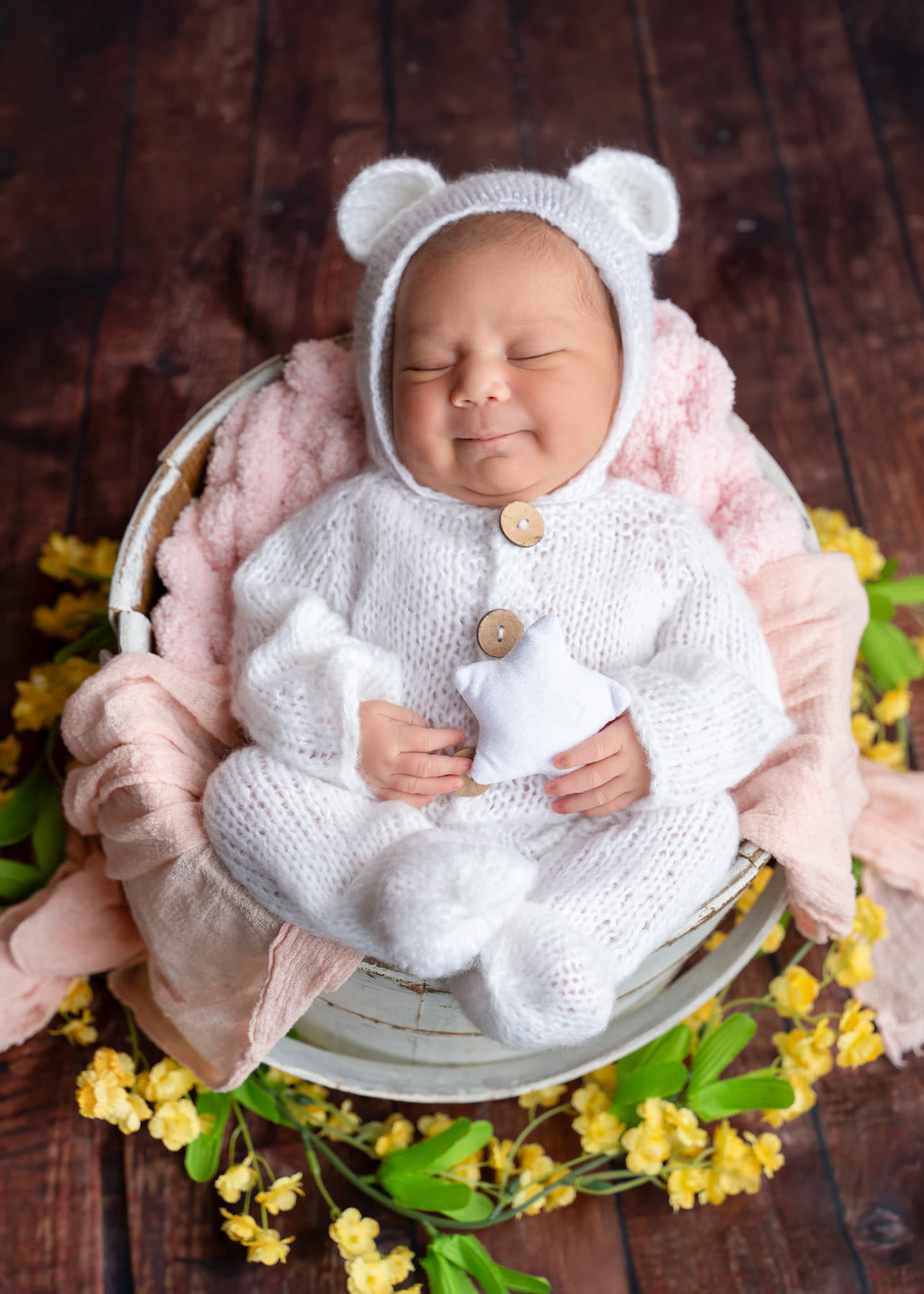 Smiling newborn in a white bear bonnet in a flower basket