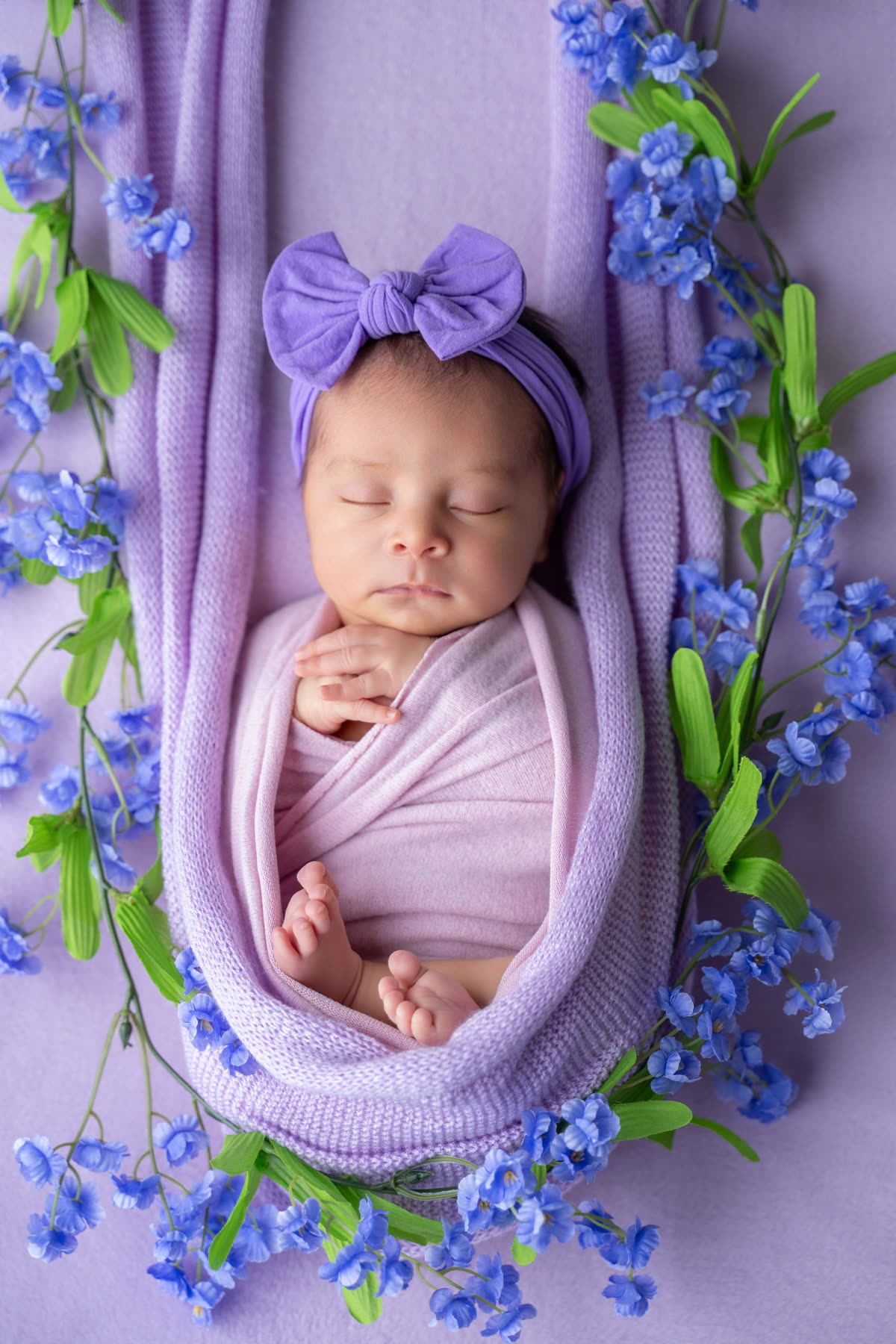 Newborn wrapped in lilac surrounded by blue flowers