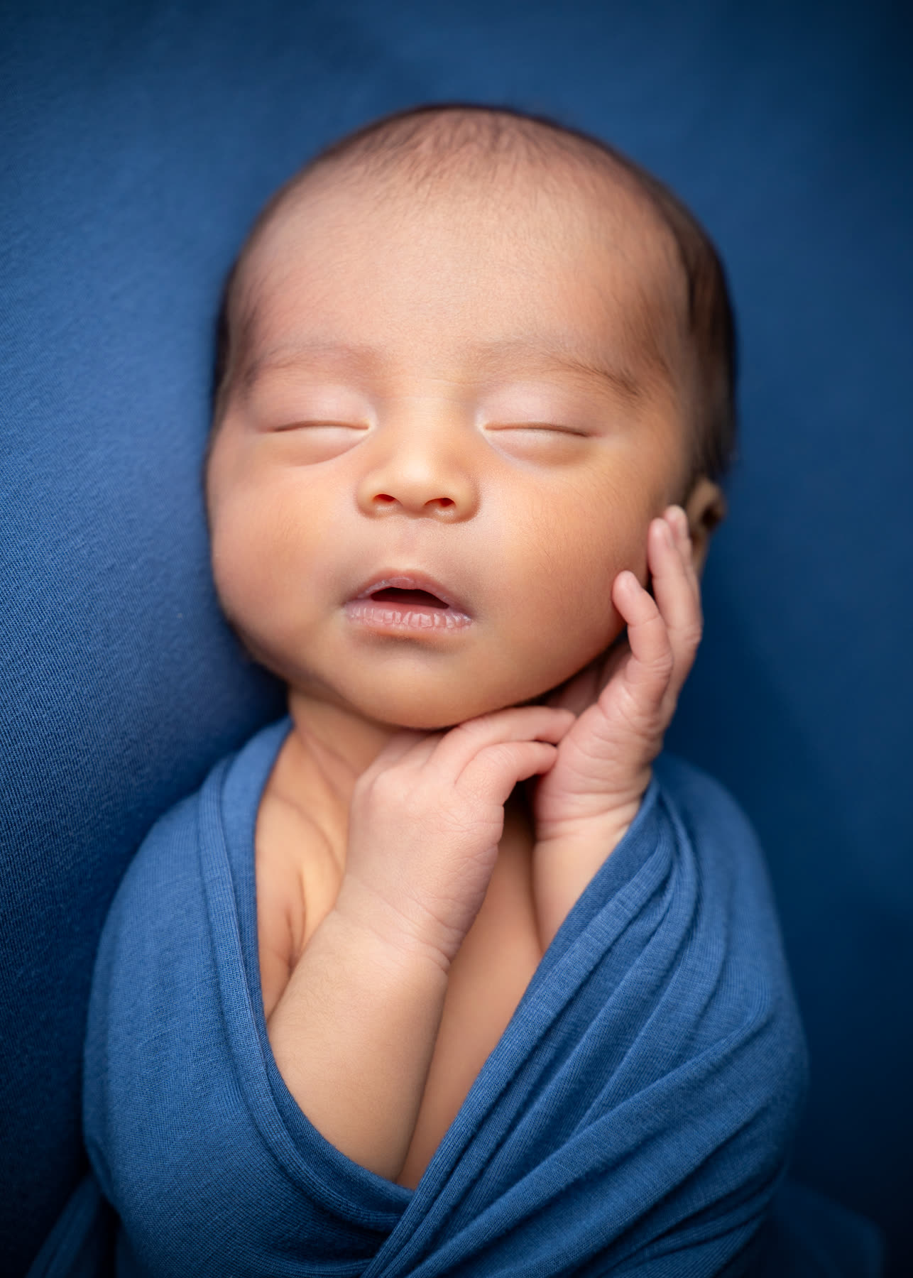 Newborn resting chin on hands against deep blue