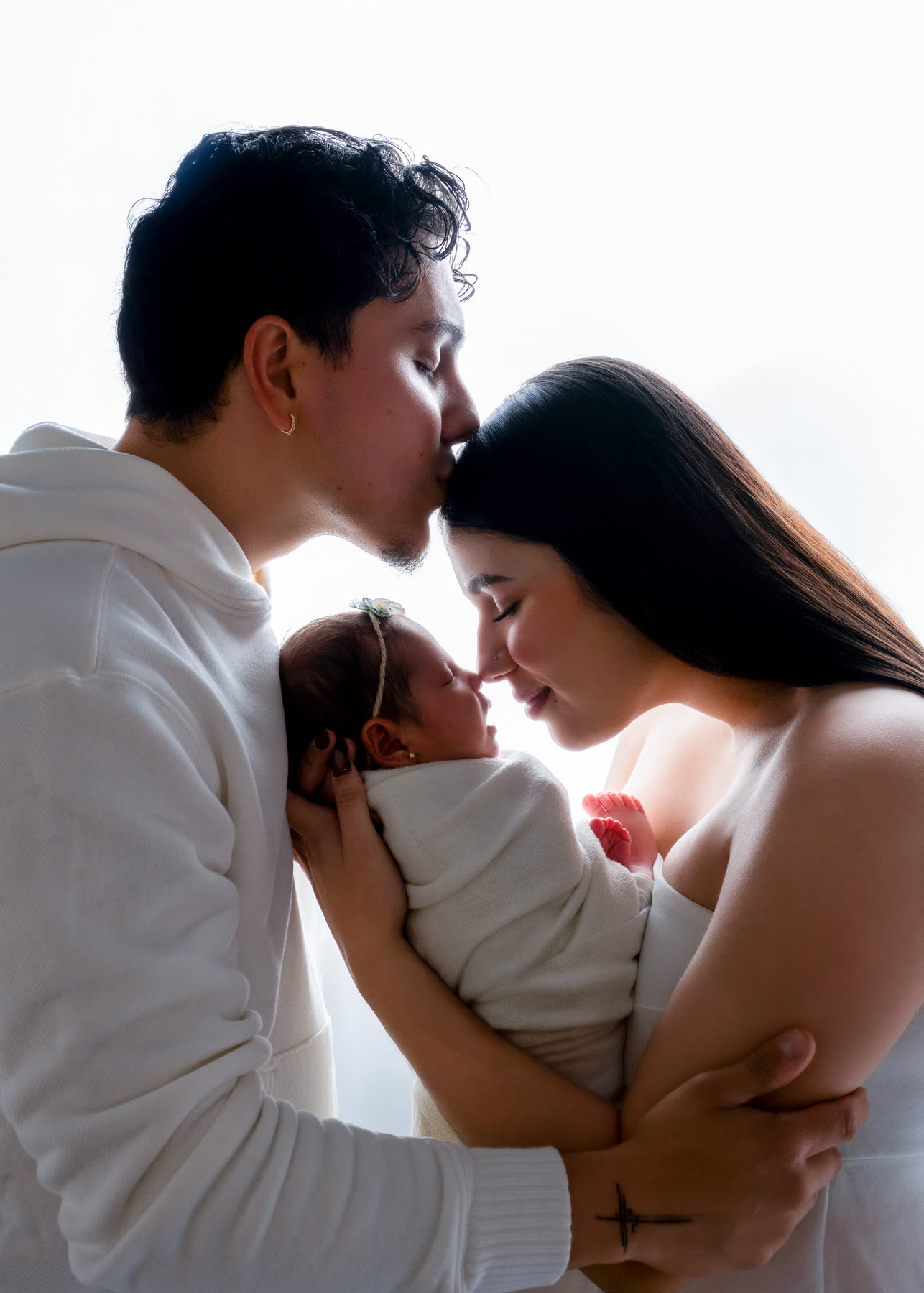 Father kissing the mother's forehead as she holds their newborn