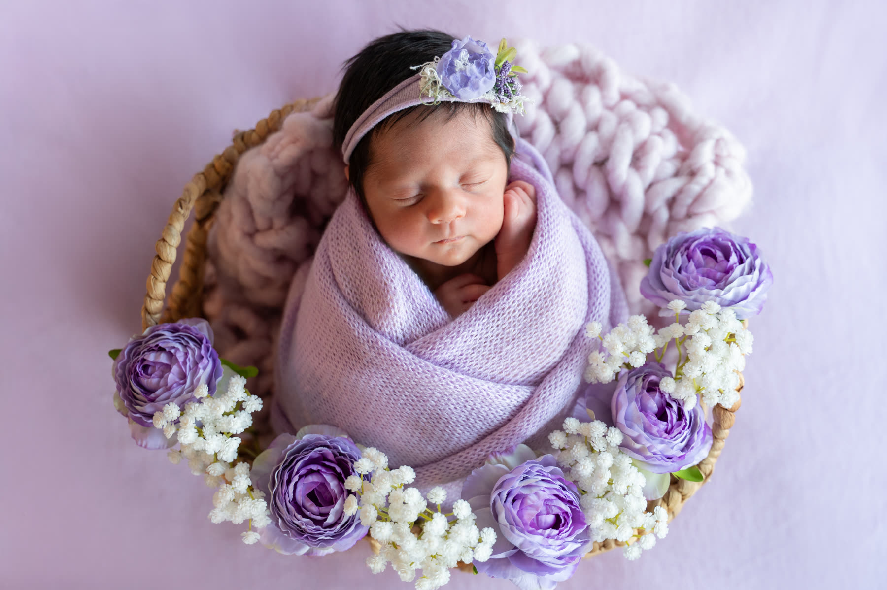 Newborn in a nest of lilac knit and purple roses