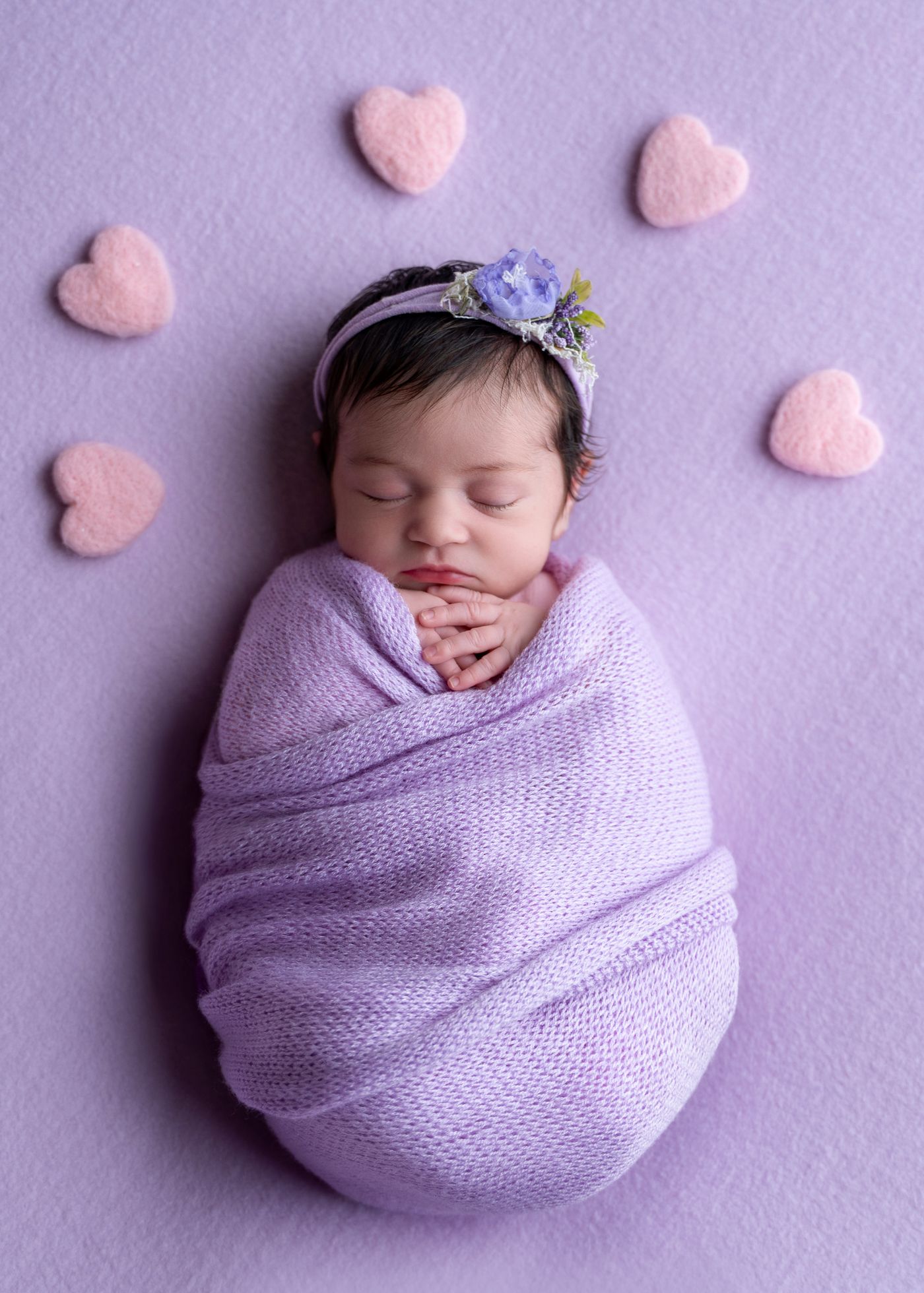 Sleeping newborn wrapped in lilac knit with felt hearts