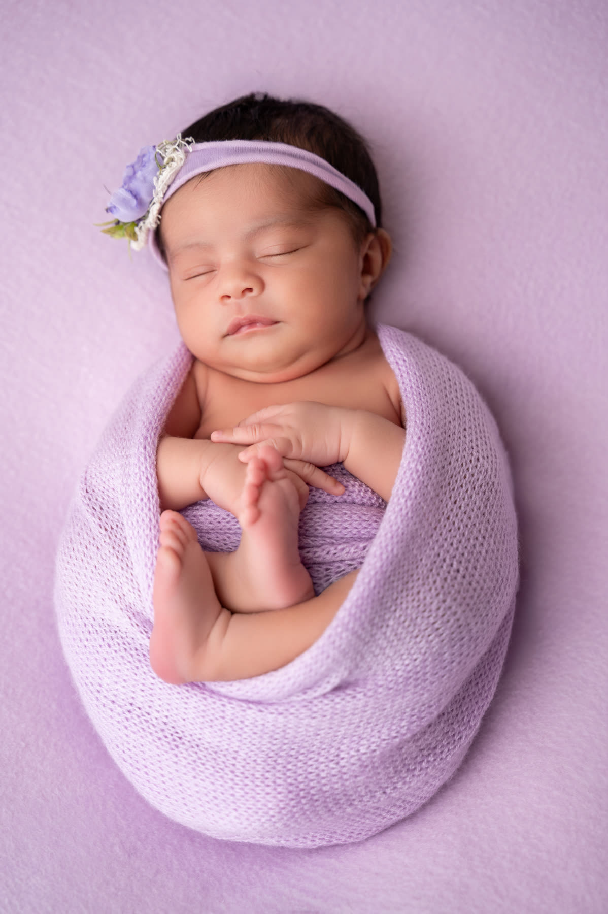 Sleeping newborn wrapped in lilac with a flower headband